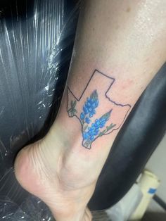 a small tattoo on the foot of a person's leg with blue flowers growing out of it