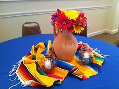 a blue table cloth with flowers in a vase on it and napkins around it