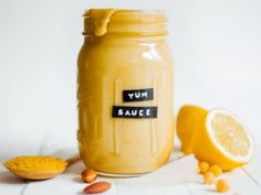 a glass jar filled with yellow liquid next to sliced lemons and peanuts on a white surface