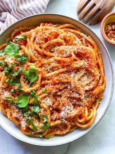 a bowl filled with pasta and sauce on top of a white table next to wooden spoons