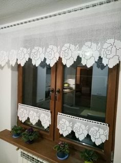 the window is decorated with white lace and potted plants