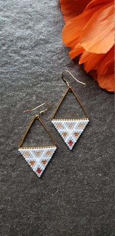 a pair of triangle shaped earrings sitting on top of a gray surface next to an orange flower