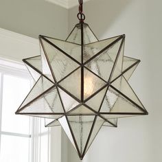 a glass star hanging from the ceiling in a room with white walls and windows behind it