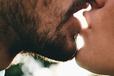 a man and woman kissing each other with their noses close to one another as the sun shines down on them