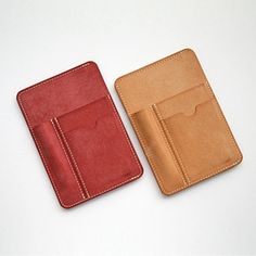 two small wallets sitting next to each other on a white surface, one is red and the other is tan