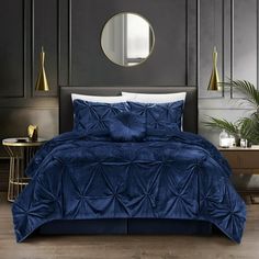 a bed with blue comforter and pillows in a dark room next to a mirror