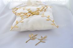 a white pillow with gold leaves on it next to a pair of golden hair pins