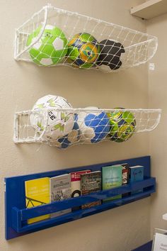 two plastic baskets are hanging on the wall above bookshelves with soccer balls in them