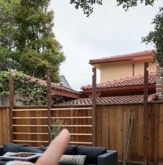 a hand pointing at a couch in front of a wooden fence and house behind it