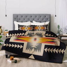 a bed covered in a black and white comforter next to a table with plants