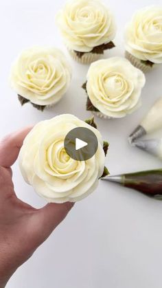 someone is holding some cupcakes with white frosting and flowers in the middle