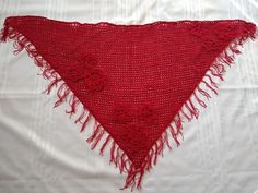 a crocheted triangle with fringes and flowers on the bottom is laying on a white sheet