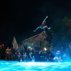 a group of people watching a man on a surfboard jump into the water at night