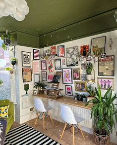 a room filled with pictures and plants on the wall next to a desk in front of a window