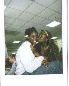 two women are hugging each other in an office cubicle, one is wearing glasses and the other has dreadlocks on her head