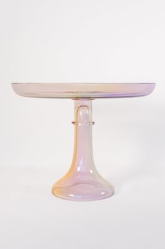 a glass cake plate sitting on top of a white tablecloth covered table with an oval shaped base