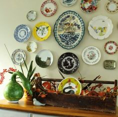 there are many plates on the wall above the dresser and vases in front of it