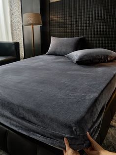 a person pointing at a bed with a black blanket on it