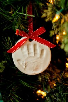 an ornament hanging from a christmas tree with a hand print on it's thumb