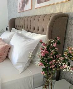 a bed with white sheets and pink flowers in a vase on the nightstand next to it