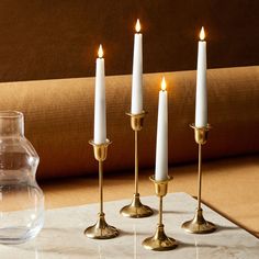 three candles are sitting on a table next to a vase with water and an empty glass