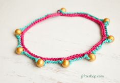 a pink and blue bracelet with gold beading on white wooden background, closeup