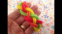 a hand is holding a multicolored rainbow loom bracelet with two gold rings