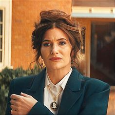 a woman wearing a suit and holding her hand up to her chest while looking at the camera