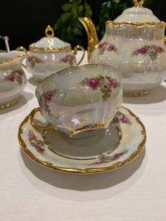 an antique tea set with pink roses on it and gold trimmings sits on a white tablecloth