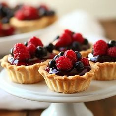 small tarts topped with berries and blueberries on a white cake plate, ready to be eaten