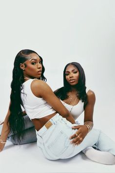 two women sitting on the ground with their arms around each other and one woman wearing jeans