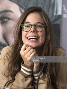 a smiling woman with glasses sitting at a table in front of a poster and microphone