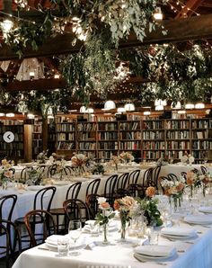 the tables are set with white linens and floral centerpieces, along with bookshelves in the background