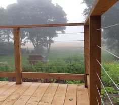 a wooden deck with a fence and cows in the distance on a foggy day