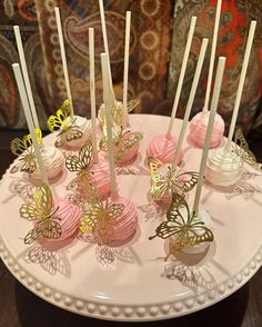 there are many pink and gold desserts on the plate with butterfly candlesticks