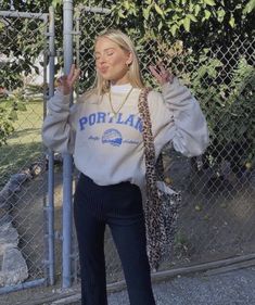 a woman leaning against a fence with her hands up to the side, wearing a sweater that says portland