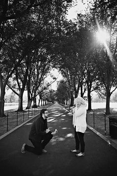 black and white photograph of two people kneeling down in the middle of a road with trees lining both sides