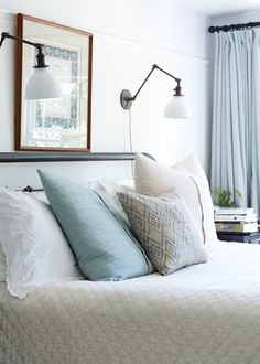 a bed with pillows and two lamps on the headboard, next to a window