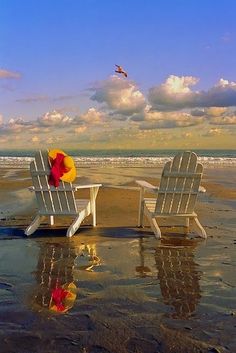 two white chairs sitting on top of a beach next to the ocean with an umbrella