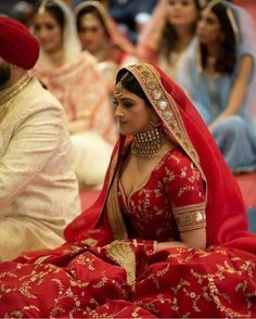 a woman in a red bridal gown sitting on the floor with other people behind her