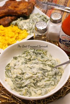 a white bowl filled with spinach and sauce next to other food on a table