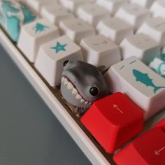 a toy shark sitting on top of a computer keyboard with its mouth open and teeth out