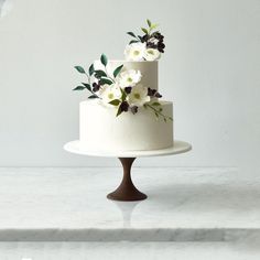 a three tiered cake with white and black flowers on the top is sitting on a marble table