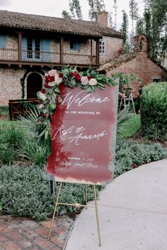 a welcome sign with flowers and greenery on it in front of a brick building