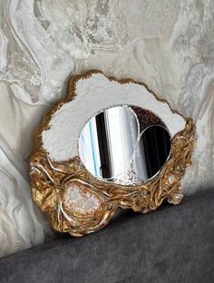 a mirror sitting on top of a couch next to a wall covered in white and gold