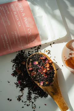 a wooden spoon filled with tea next to a bag of loose black tea