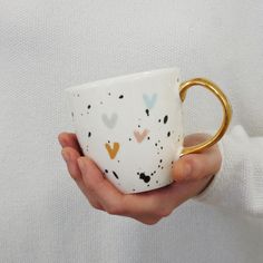 a hand holding a coffee cup with hearts painted on the outside and gold rimmed