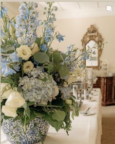 a blue and white vase filled with lots of flowers on top of a long table