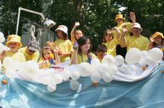 a group of children in yellow shirts and white hats are standing behind a large balloon float