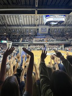 a crowd of people at a basketball game raising their hands in the air to catch a ball